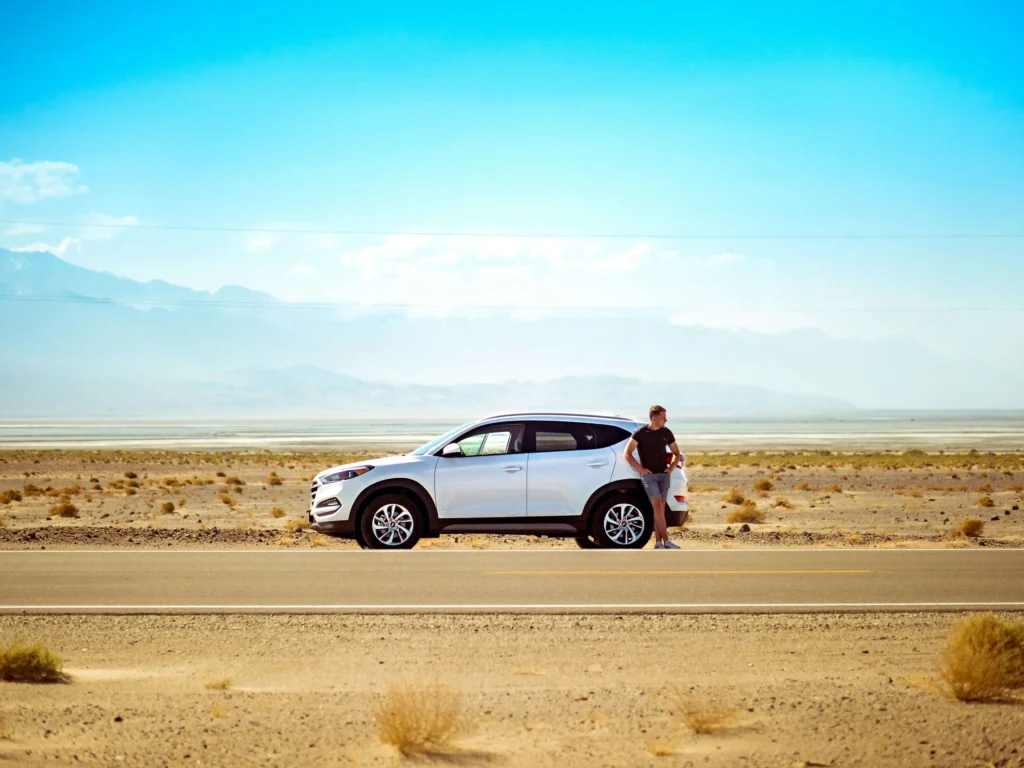 A man has his car windows tinted and is standing in deserted aread.