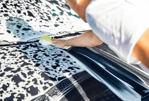 A man tinting and cleaning car windows using the right window tint kit for car.